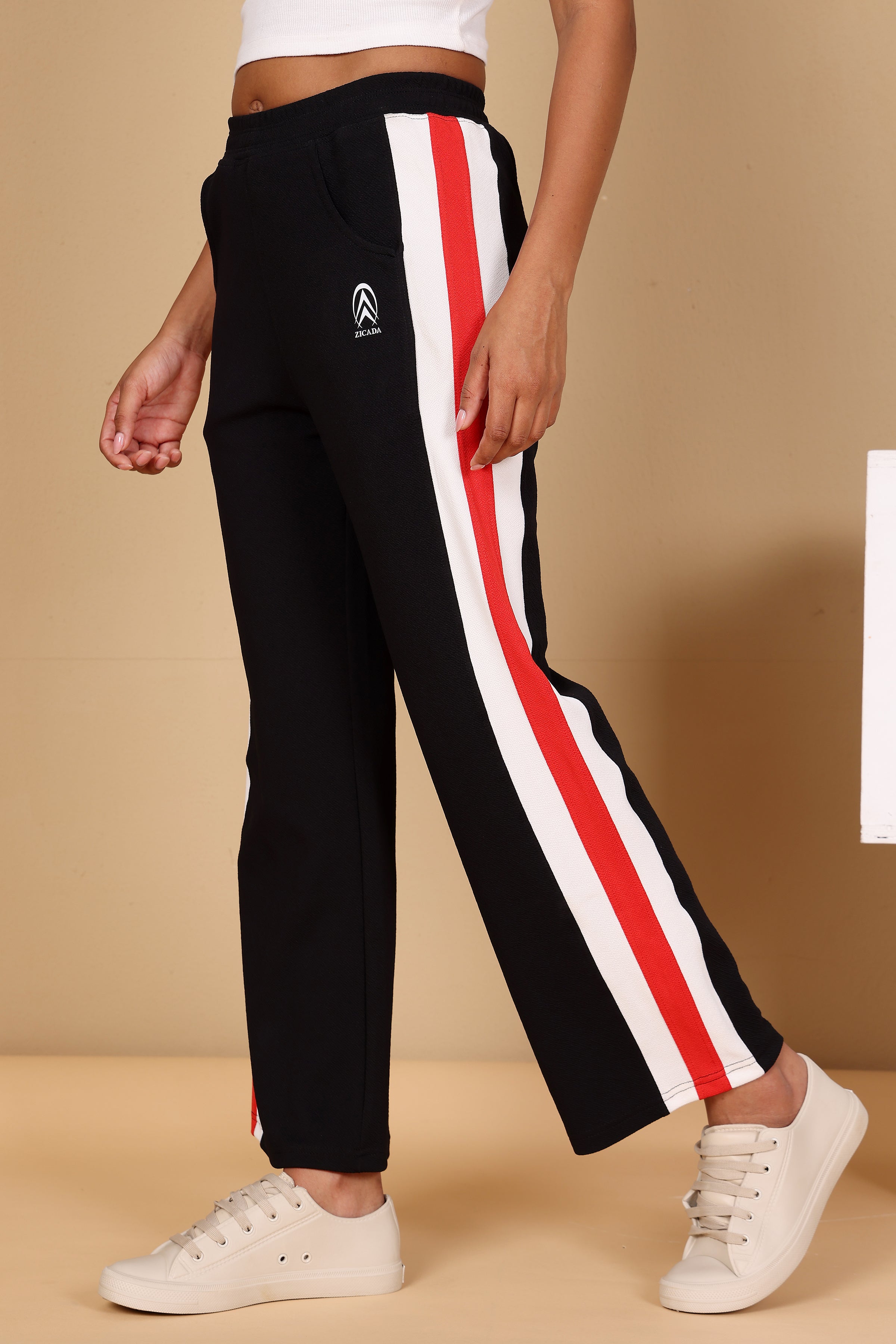 Black track pants with red and white stripes worn by a person on a beige background