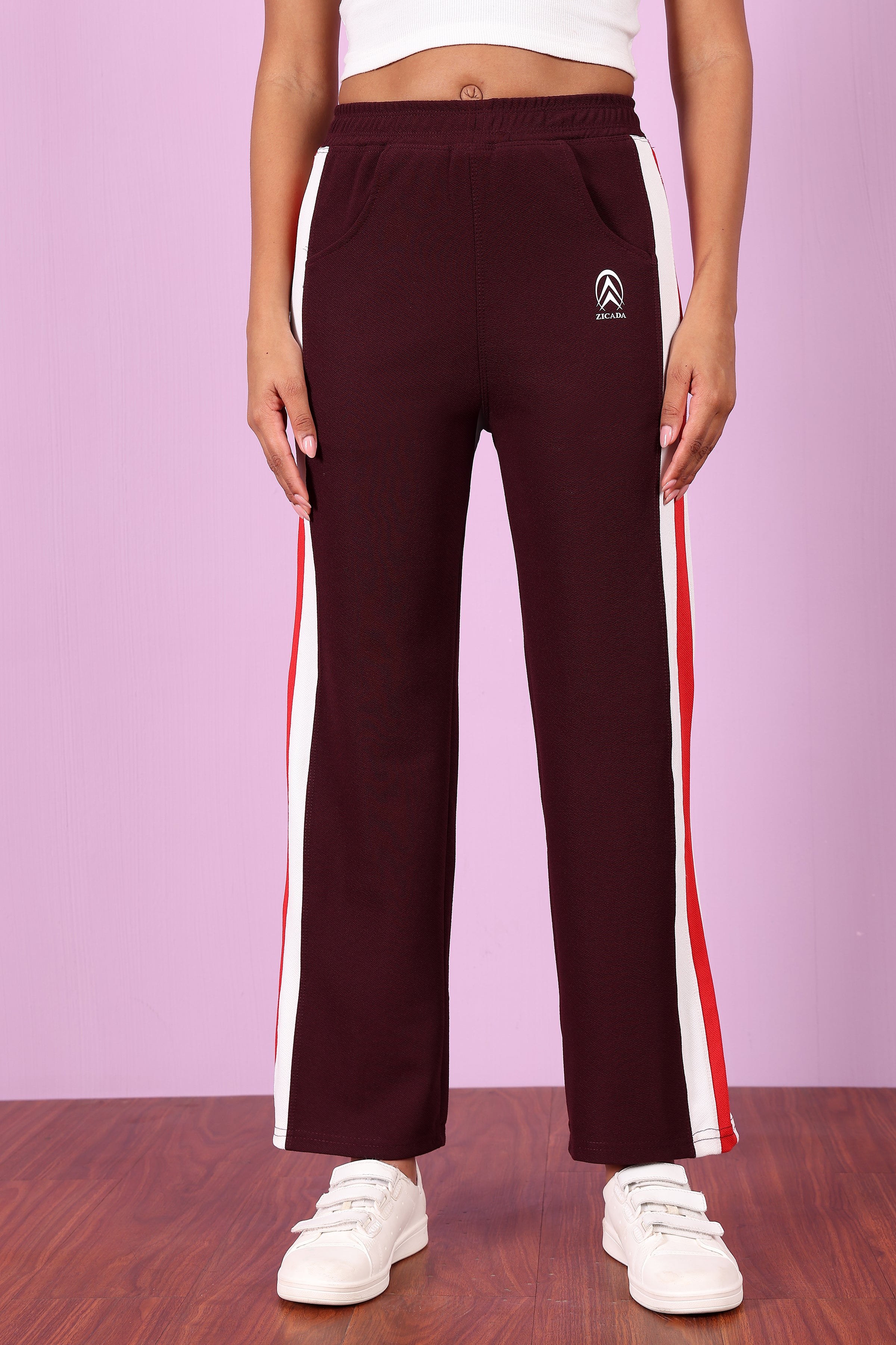 ZICADA's Maroon track pants with white and red stripes worn by a person on a purple background