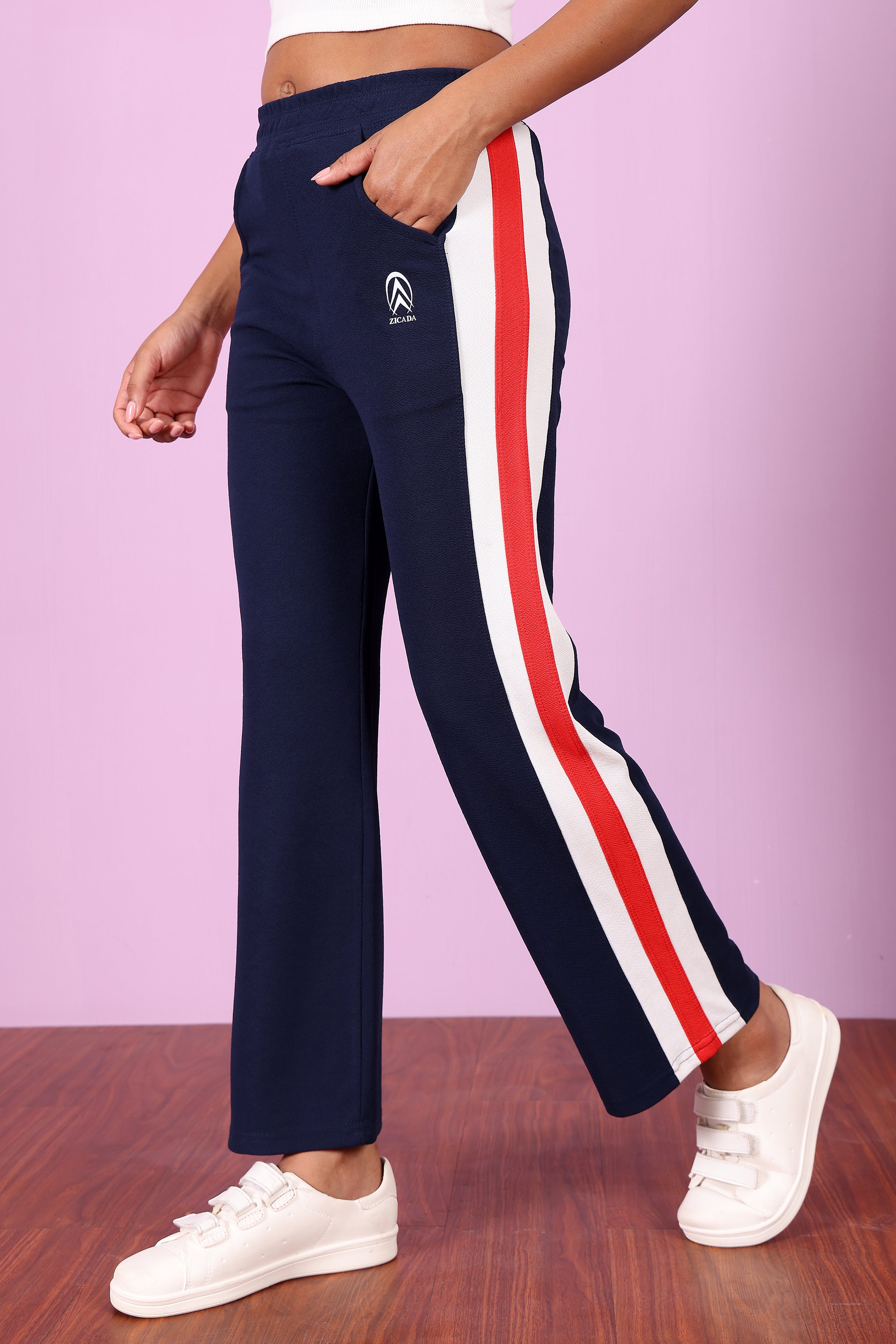 Zicada Navy track pants with red and white stripes worn by a person on a pink background